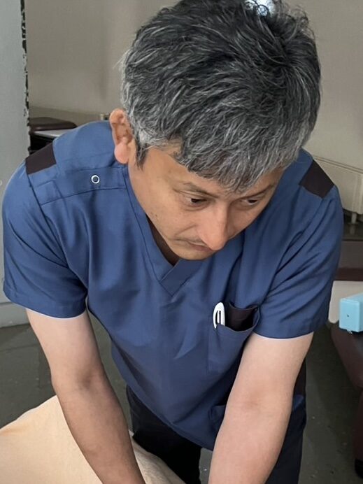 青い施術着で身体の状態を確認する院長
